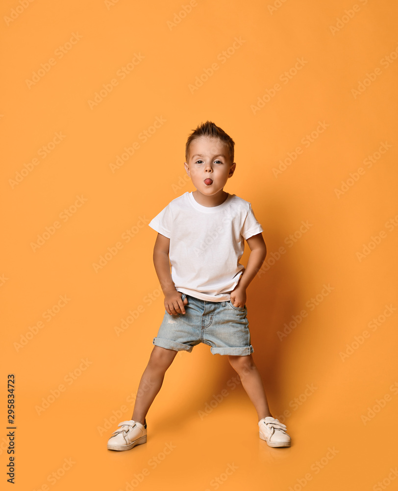 Playful kid boy bully in white t-shirt and blue jeans shorts is sticking out his tongue teasing us, ready to run off Playful kid boy bully in white t-shirt and blue jeans shorts is sticking out his tongue teasing us, ready to run off