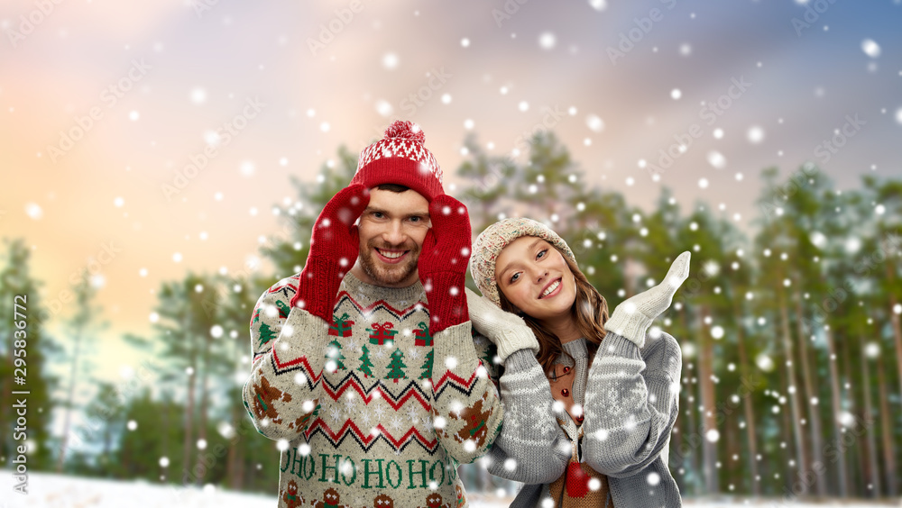 christmas, clothes and holidays concept - portrait of happy couple in ugly sweaters over winter park background christmas, clothes and holidays concept - portrait of happy couple in ugly sweaters over winter park background