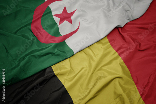 waving colorful flag of belgium and national flag of algeria.