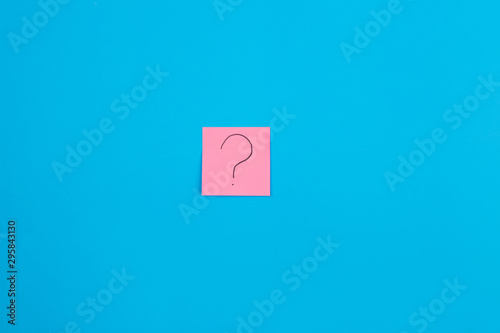 Photo of a pink sticker with a question mark placed in the center of a blue background. Close-up. Place for advertising. Stickers.