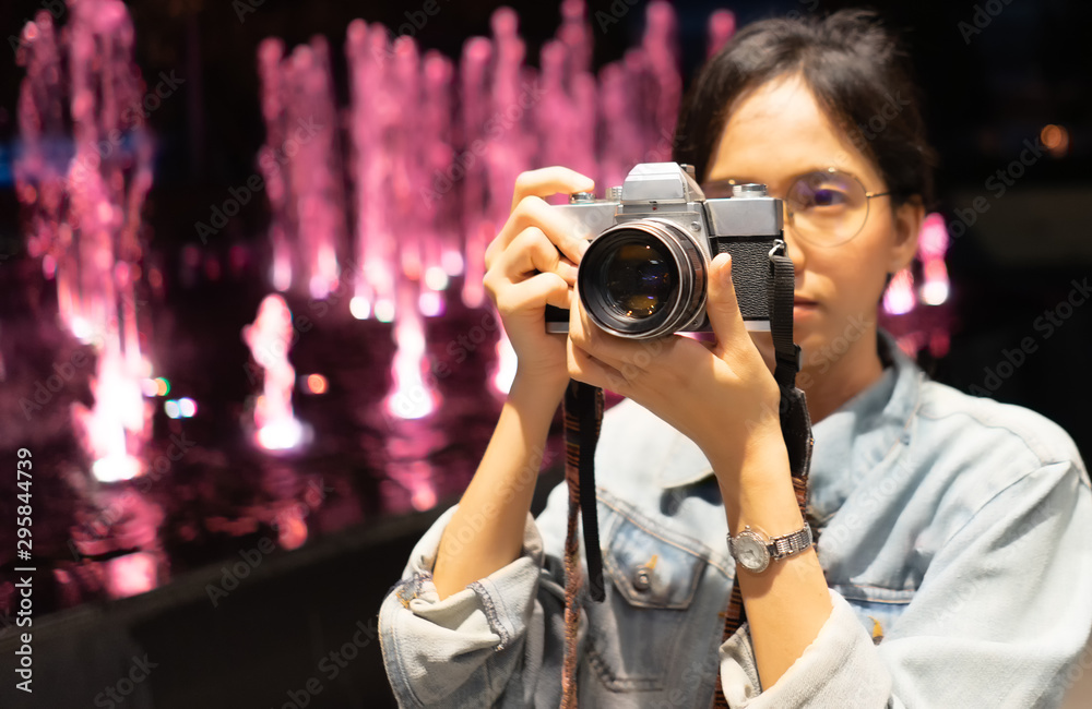 girl photographer In the jean coat take picture at the night with Vintage Film camera .Behind is a fountain.