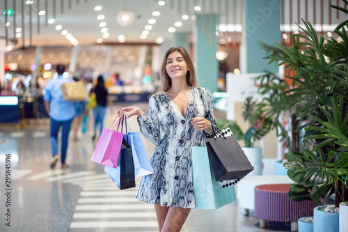 A sweet smiling girl is walking around the mall, carrying a large number of shopping bags in shis hands, expressing an emotion of joy. The concept of shopping. Day of discounts.