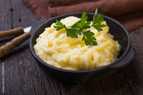 Mashed potatoes or boiled puree with parsley  in cast iron pot on dark wooden rustic background.  top view photo