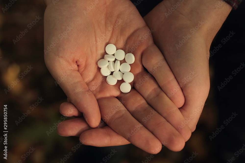 Closeup of a man holding white pills im his hands with dry leaves in the background. Concept of supplementation in autumn. Closeup of a man holding white pills im his hands with dry leaves in the background. Concept of supplementation in autumn.