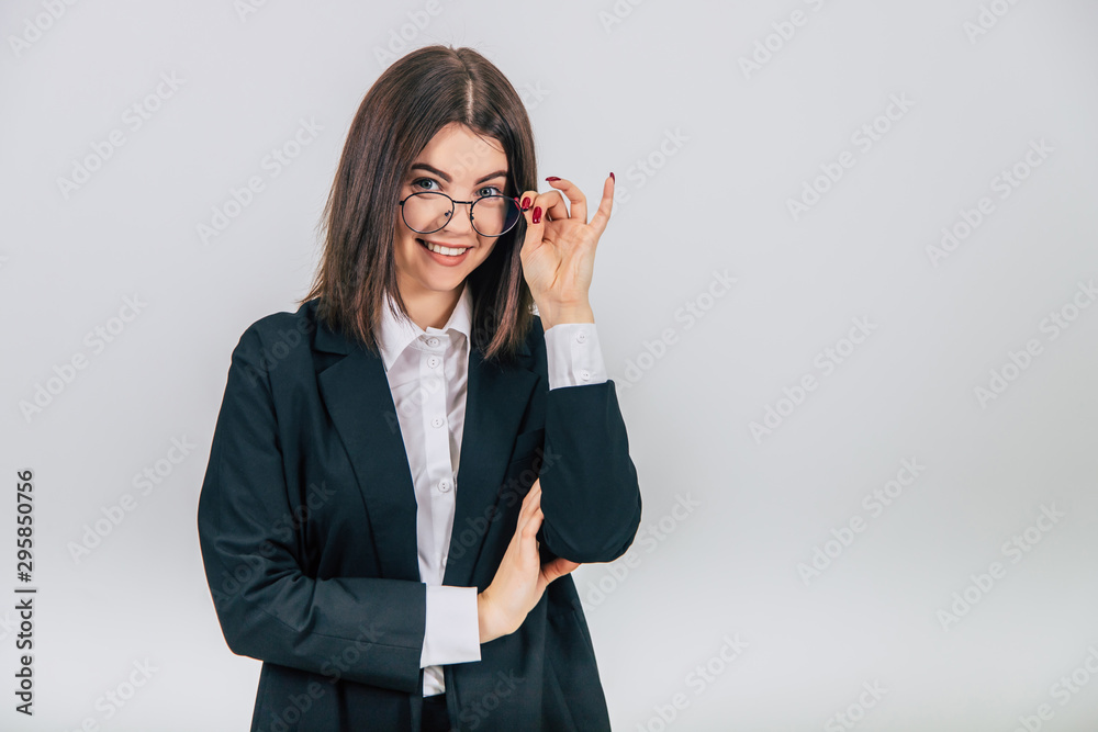 Young businesswoman in black suit standing, keeping her hand on the glasses, looking at the camera, smiling. Young businesswoman in black suit standing, keeping her hand on the glasses, looking at the camera, smiling.