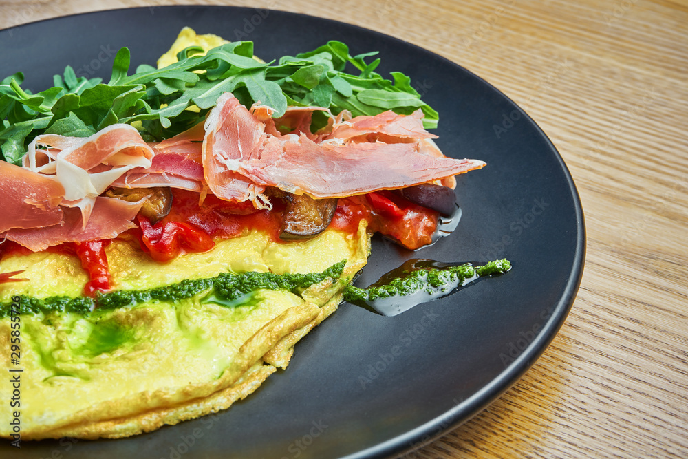 Frittata with prosciutto, pesto sauce, arugula and bell pepper on black plate. Tasty and healthy lunch. Omelette