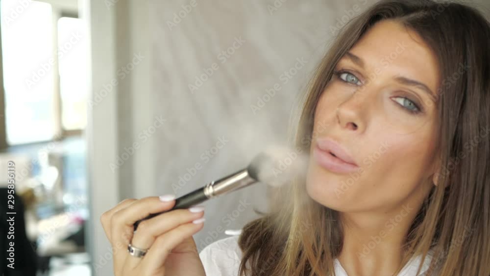 Girl blowing on makeup brush with powder. Girl blowing on makeup brush with powder.