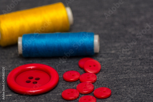 Colorful bright threads for sewing and red buttons. Gray blurred background. Sewing industry. Atelier design elements.