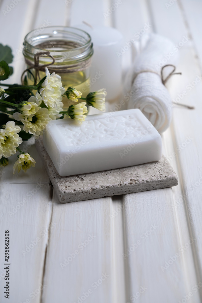 Handmade soap with a pattern lies on the table. On a white table is handmade soap, flowers and olive oil. Collection of items for the bathroom