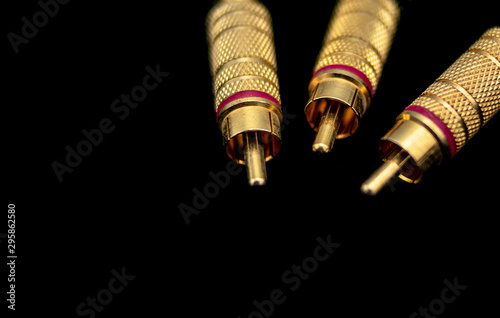 Three male metallic and gold rca type connectors without cables over black foreground photo