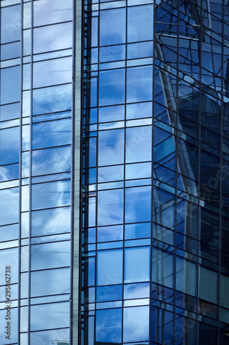 Windows of a skyscraper with reflection of blue sky and white clouds. A fragment of a glass facade of a modern office building in a business district of a city. Geometric shapes in modern architecture