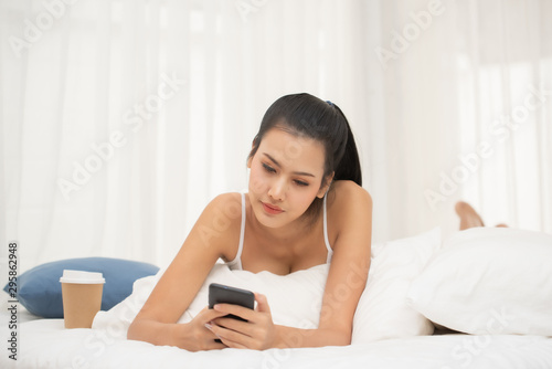 Young Woman Using Mobile Phone While Lying On Bed At Home