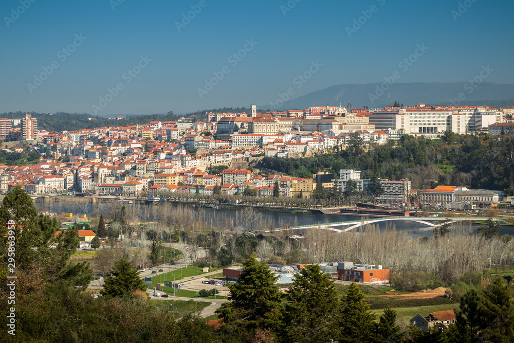 View of the city of Coimbra in Portugal, from downtown to high with the University, also with the Mondego river and the pedestrian bridge Pedro e Inês in the foreground.