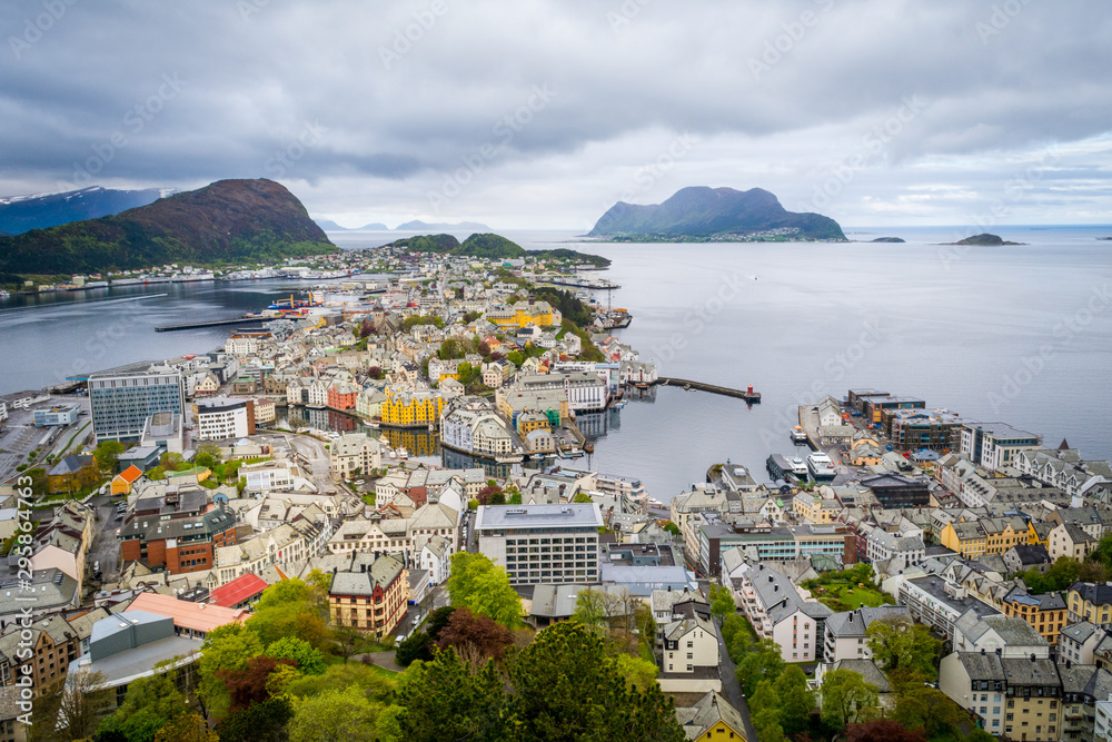 Obraz premium Skyline and cityscape of Alesund, Norway, on a cloudy day. Ocean bay in the background, bright houses and architecture in the foreground. Aerial view. 
