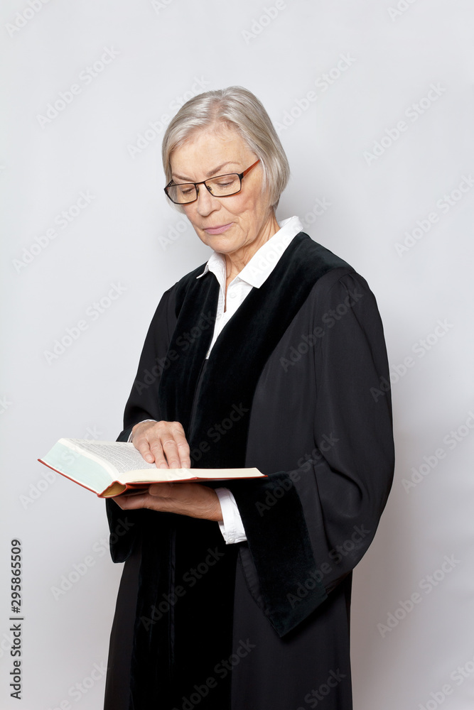 German jurisdiction concept: elderly judge in black robe reading in a book with the text of the german constitution. German jurisdiction concept: elderly judge in black robe reading in a book with the text of the german constitution.