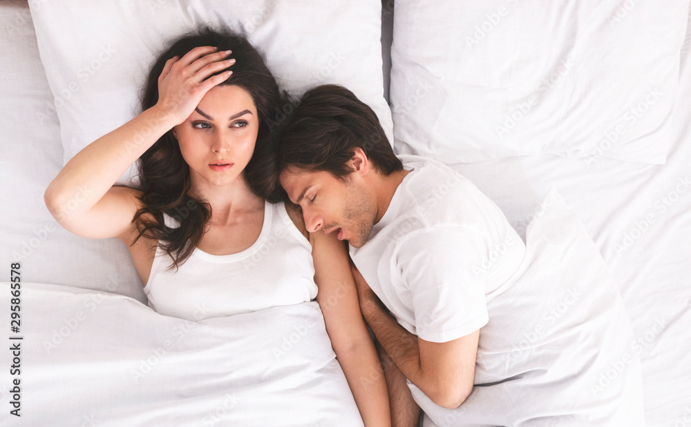 Grumpy woman with insomnia lying with man in bed - obrazy, fototapety, plakaty 
