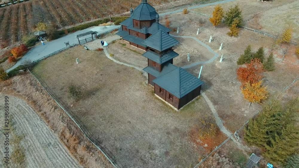 Wooden church and mills aerial view. The drone takes off from the heights of an old black wooden church and mills in the fall in a field on the hills overlooking the lake. Wooden church and mills aerial view. The drone takes off from the heights of an old black wooden church and mills in the fall in a field on the hills overlooking the lake.