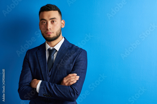 Portrait of serious handsome successful kazakh asian businessman in suit with arms crossed on blue studio background , isolated with copy space