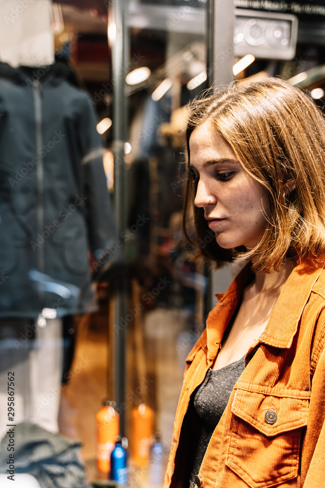 Vertical photo of a blonde girl looking at the window of a fashion store