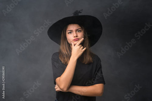 Girl with witch costume for halloween parties over isolated dark background thinking an idea