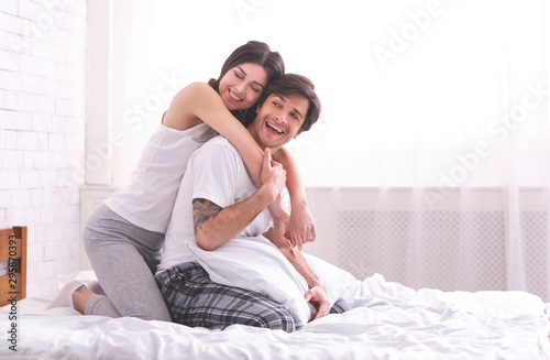 Smiling girl embracing her boyfriend back in bed