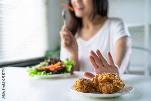 Woman on dieting for good health concept, young women use hands to push fried chicken and choose to eat vegetables for good health.