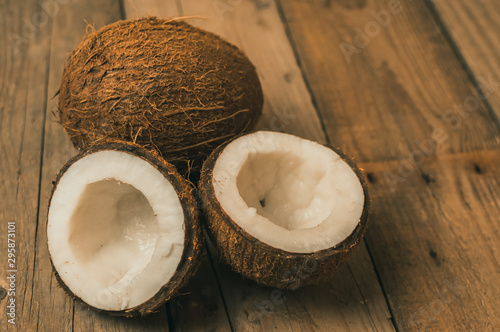 tropical coconut fruits on a wooden background in rustic style. One nut is whole, the second is broken into 2 parts in the shell. Template for design. Copy space.