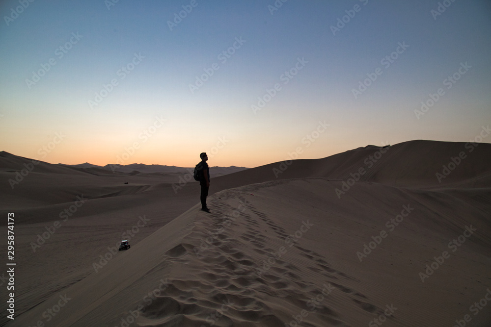 young man on sand in a desert near Huacachina, Ica region, Peru. The sunset desert view