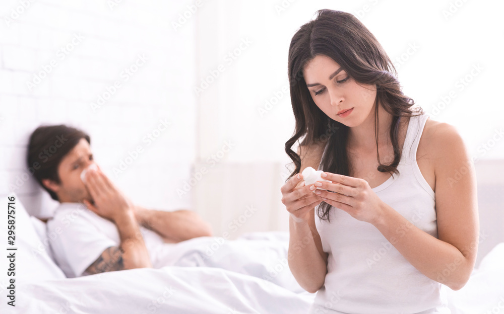 Attentive girl bringing medicaments to sick boyfriend lying in bed