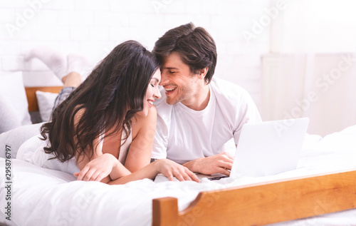 Loving spouses bonding, using laptop in bed