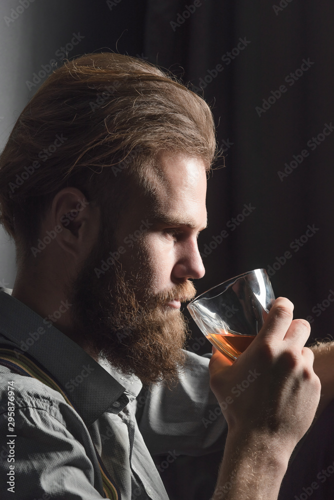 Portrait of a handsome young man with a beard drinking alcohol from a glass. Portrait of a handsome young man with a beard drinking alcohol from a glass.