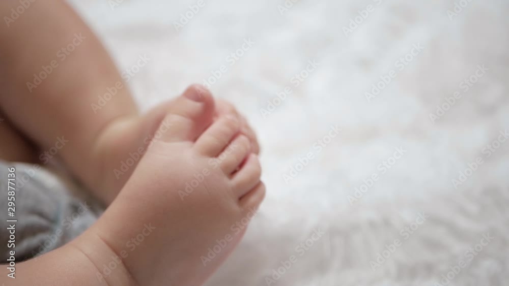Beautiful cute little baby legs are touching each other. Child is on white bedspread. Close-up Beautiful cute little baby legs are touching each other. Child is on white bedspread. Close-up