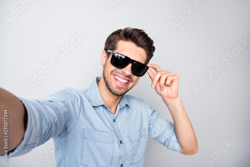 Photo of cheerful positive handsome attractive man taking selfie recording video smiling toothily isolated over grey color background wearing sunglass © deagreez