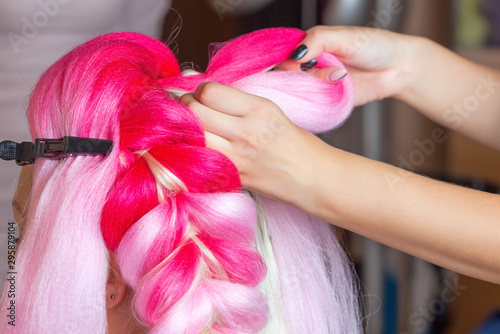 The hairdresser weaves braids with pink kanekalons beautiful blonde beauty salon.Beautiful hairstyles. photo