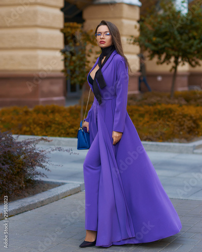 Young beautiful caucasian woman with long straight hair and makeup in purple trousers and long coat cape standing and posing at city street in autumn photo