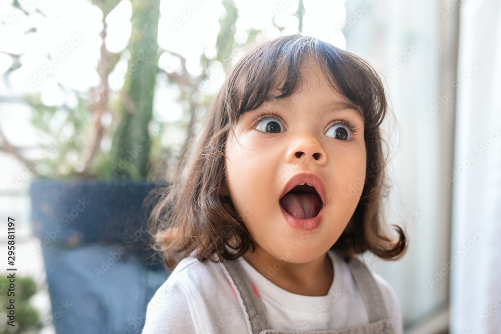 Cute little girl looking surprised while playing at home - obrazy, fototapety, plakaty 