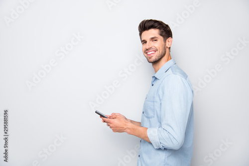 Profile side photo of positive cheerful man using holding his mobile phone have online conversation with friends on social media at copyspace wear stylish outfit isolated over grey color background