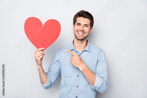 Portrait of charming man with positive emotions expression hold hand red big paper card heart present his gift for 14-february to girlfriend wear casual style clothes isolated grey color background