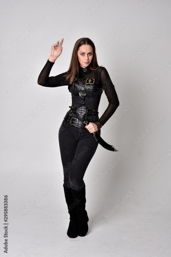 full length portrait of a pretty brunette woman wearing black leather fantasy costume with a dagger. standing pose on a studio background. full length portrait of a pretty brunette woman wearing black leather fantasy costume with a dagger. standing pose on a studio background.