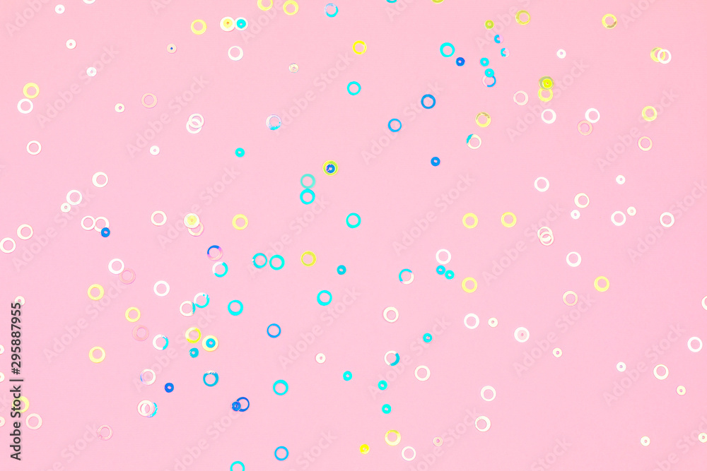 Colorful holographic foil confetti background. Pastel colored pink, blue and yellow circles sparse on trendy soft pink colored paper. Simple holiday concept. Top view, flat lay.
