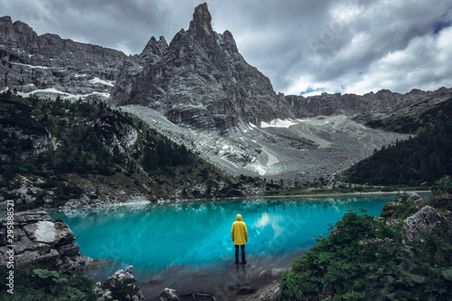 Man in yellow jacket standing alone on the rock at alpine lake Lago di Sorapis in the Italian mountains - Dolomites