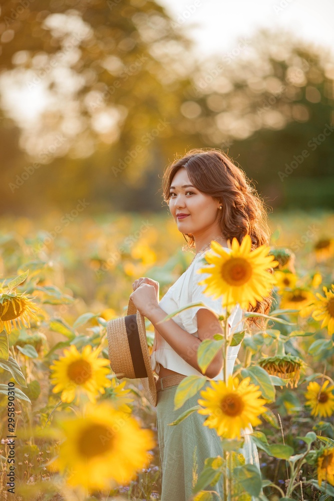 Young Asian woman with curly hair in a field of sunflowers at sunset. Portrait of a young beautiful asian woman in the sun. Young Asian woman with curly hair in a field of sunflowers at sunset. Portrait of a young beautiful asian woman in the sun.