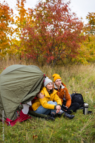 trekking and hiking concept - happy couple in love sitting near green tent in autumn forest