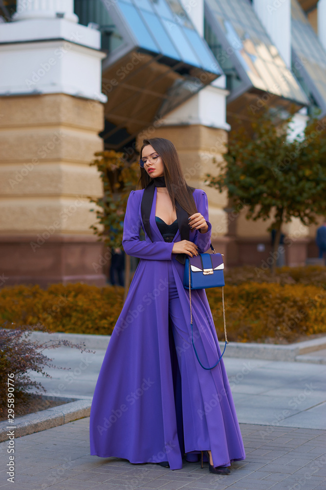 Young beautiful caucasian woman with long straight hair and makeup in purple trousers and long coat cape standing and posing at city street in autumn Young beautiful caucasian woman with long straight hair and makeup in purple trousers and long coat cape standing and posing at city street in autumn