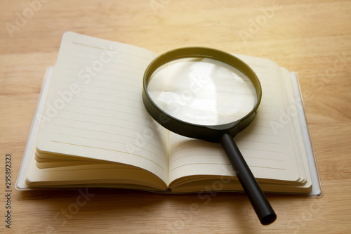 opened notebook and magnifier glass on the wooden table