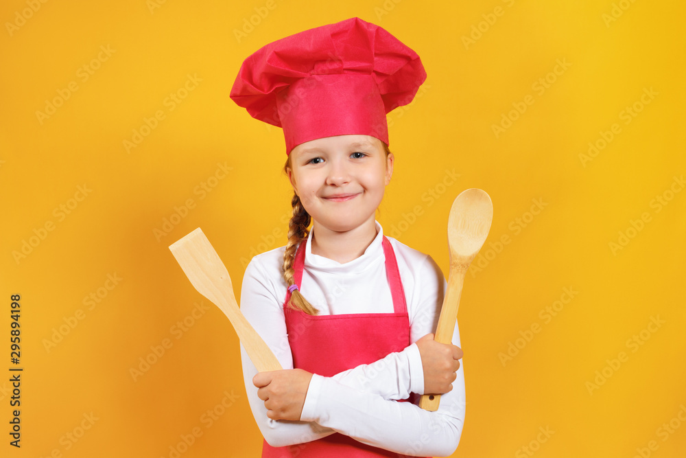 Beautiful little girl chef on a yellow background. The child holds in his hands a wooden spoon and spatula Beautiful little girl chef on a yellow background. The child holds in his hands a wooden spoon and spatula