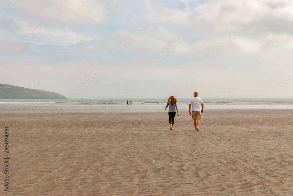 One man and a woman walking on sandy beach. One father and his daughter enjoying the day. family.