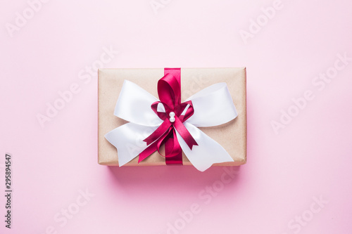 Gift or present box with a big bow on a pink table top view. Flatlay composition for Christmas birthday, mother day or wedding.