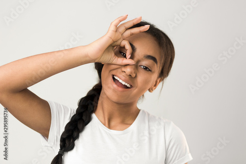 Afro girl holding okay gesture near eye, making glasses