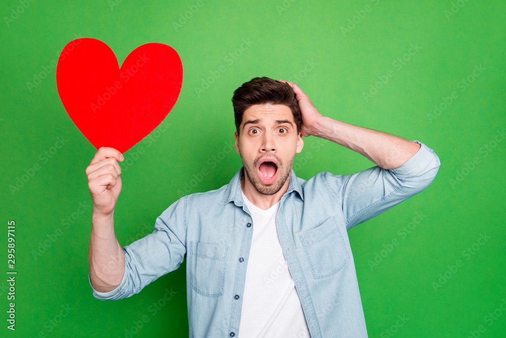 Photo of amazing guy holding big red paper heart forgot about romance surprise for girlfriend open mouth wear denim shirt isolated green color background Photo of amazing guy holding big red paper heart forgot about romance surprise for girlfriend open mouth wear denim shirt isolated green color background